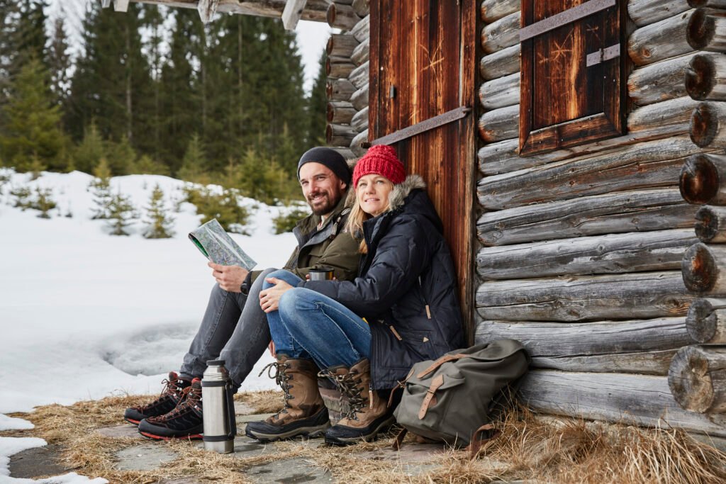 Portrait of couple reading map sitting outside log cabin in winter, Elmau, Bavaria, Germany